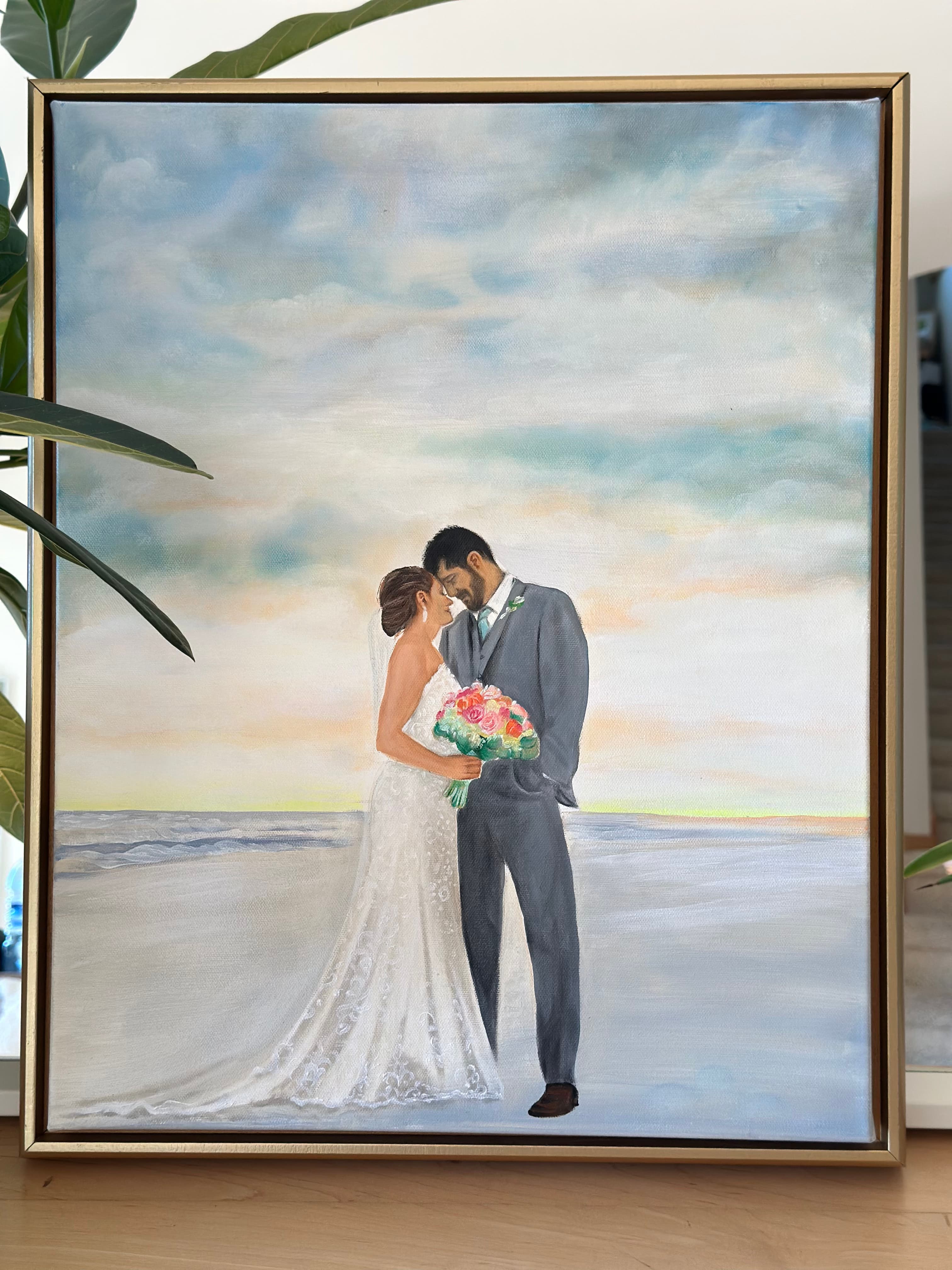 Beautiful beach sunset wedding painting — the couple on the sand beneath pastel sunset clouds, in a gold floater frame